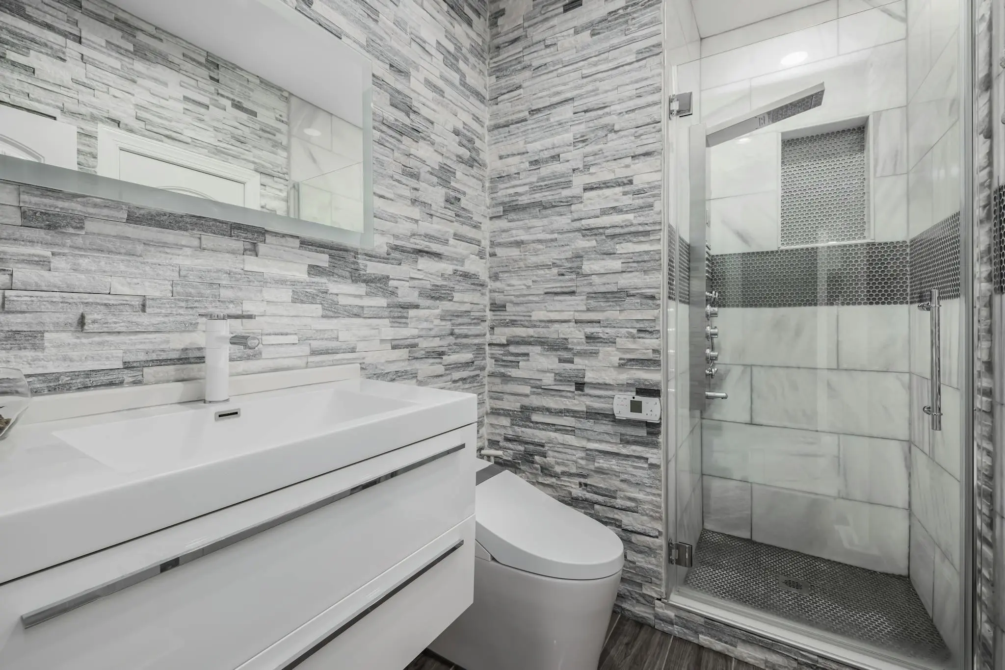 Stylish modern bathroom featuring a glass shower, stone walls, and sleek white vanity.